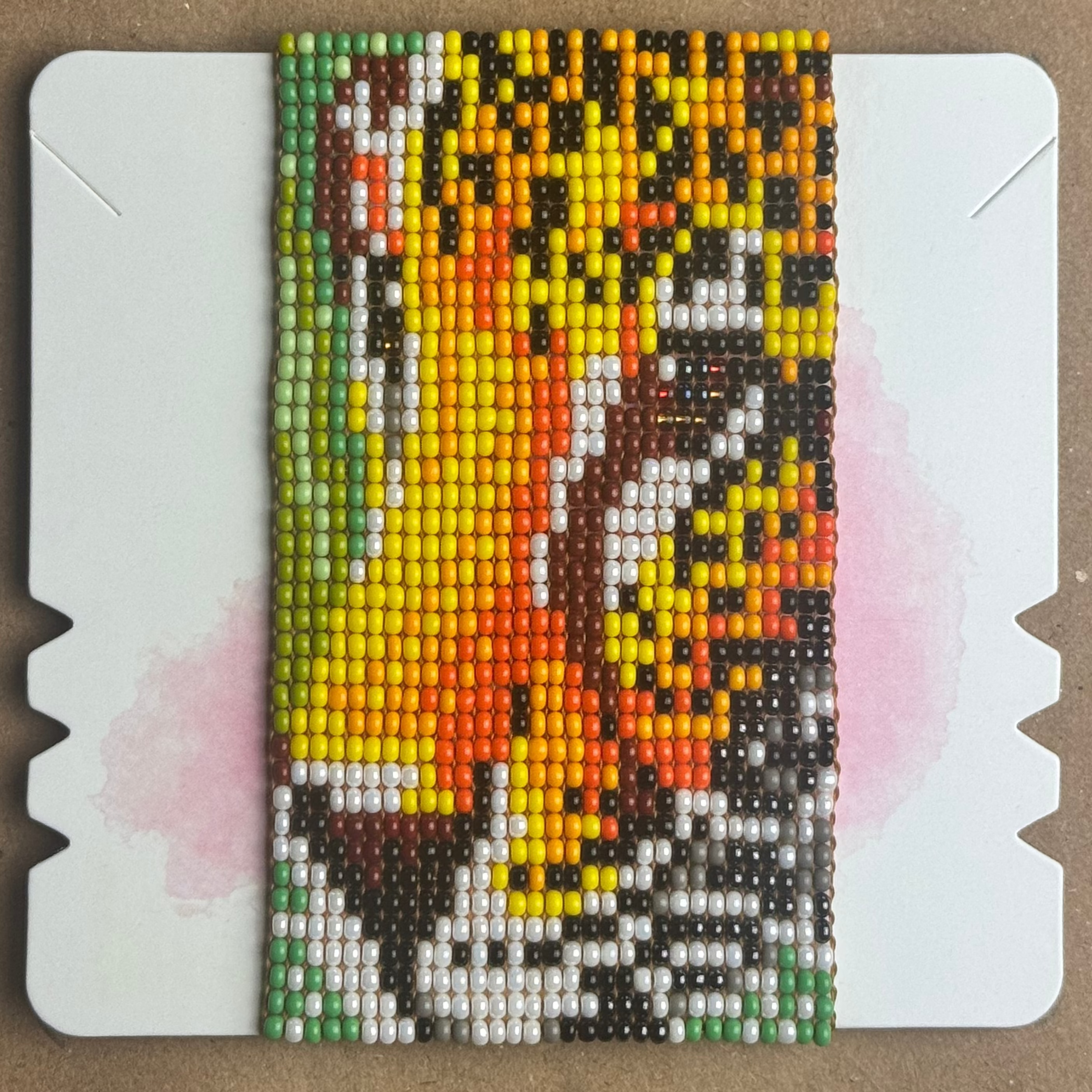A colorful diamond painting canvas featuring a stylized portrait of a jaguar, made with small beads, displayed on a white mounting board over a brown cardboard background.